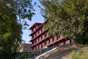  Ein charakteristischer Holzbau mit ortstypischen geschosshohen konstruktiven Holzschutzelementen, die das Gebäude horizontal strukturieren und die roten lasierten Schalungen entsprechend schützen. 