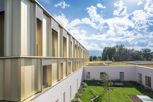  Die Fassade ist modular aufgebaut, tiefe Kastenelemente und Fenster wechseln einander ab. Sie reichen bis zum Boden und sollen die optische Nähe nach draußen zum Grün vermitteln. Ihre Rahmen sind mit goldenem Aluminum eloxiert – ebenfalls eine optische Maßnahme, um das Gebäude für Kinder und Jugendliche möglichst angenhem erscheinen zu lassen 