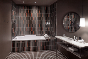  Badezimmer einer Suite: Rötlich-braune bis schwarze Wand- und Bodenfliesen greifen die Keramikfassade des Gebäudesockels auf  