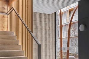  Die Treppenhäuser zeigen einen gelungenen Übergang der Materialien. Am Boden ein klassisches Straßenpflaster, an den Wänden kannelierter Beton, der die Lamellenstruktur der Absturzsicherung aus Holz und der Metall­decke aufgreift 