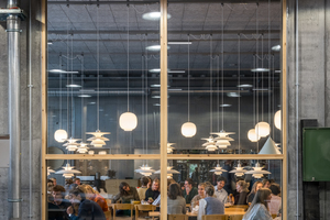  Durchblicke auch innerhalb des Gebäudes sind ein durchgängiges Prinzip in der Hochschule. So gibt es zwischen der zentralen Cafeteria und der direkt anschließenden Holzwerkstatt in der Stahlbetonwand eine riesige 10 cm starke Glasscheibe. Sie ermöglicht einen Einblick, lässt aber keinerlei Geräusche durch  