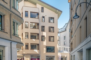  Das Apartmenthaus Vera in Andermatt ist ein gelungenes Beispiel für die Symbiose von traditioneller Schweizer Chalet-Architektur und zeitgenössischem Design. Mit seiner geschwungenen, goldfarbenen Holzfassade und dem massiven Natursteinsockel fügt es sich harmonisch in die alpine Umgebung ein 