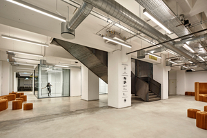  Der Eingangsbereich im Erdgeschoss ist ganztägig frei zugänglich. Hinter der Stahltreppe fällt der Blick auf die verglasten Studioboxen 