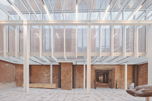  Der Anschluss an den Bestand ist eine kunstvolle Glasfuge, die als solche gar nicht in Erscheinung tritt. Die Konstruktion des gläsernen Übergangs gliedert den Raum des Westhofs und schafft eine sinnvolle Zonierung vor dem Rundgang. Tageslicht über altem Pflasterboden ist ein zusätzlicher Gewinn 