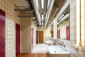  Der Kontrast zwischen alten und neuen Bauteilen wird in den Sanitärräumen besonders sichtbar. Die violetten Türen stammen aus dem Bestand, während die Holztüren neu ergänzt wurden 