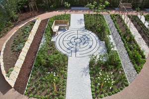  Hinter dem Gebäude befindet sich ein Garten mit Hochbeeten und Aufenthaltsmöglichkeiten. Die Wege bieten unterschiedliche Bodenbeläge  