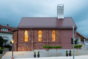  Die Architekten verwenden beim Anbau lange, geschnittene Quader. Am Übergang von Neu- zu Altbau steht die Holzkonstruktion aus Furnierschichtholz. Der über den Dachfirst ragende Kirchturm markiert diese Stelle und macht sie nach Außen sichtbar 